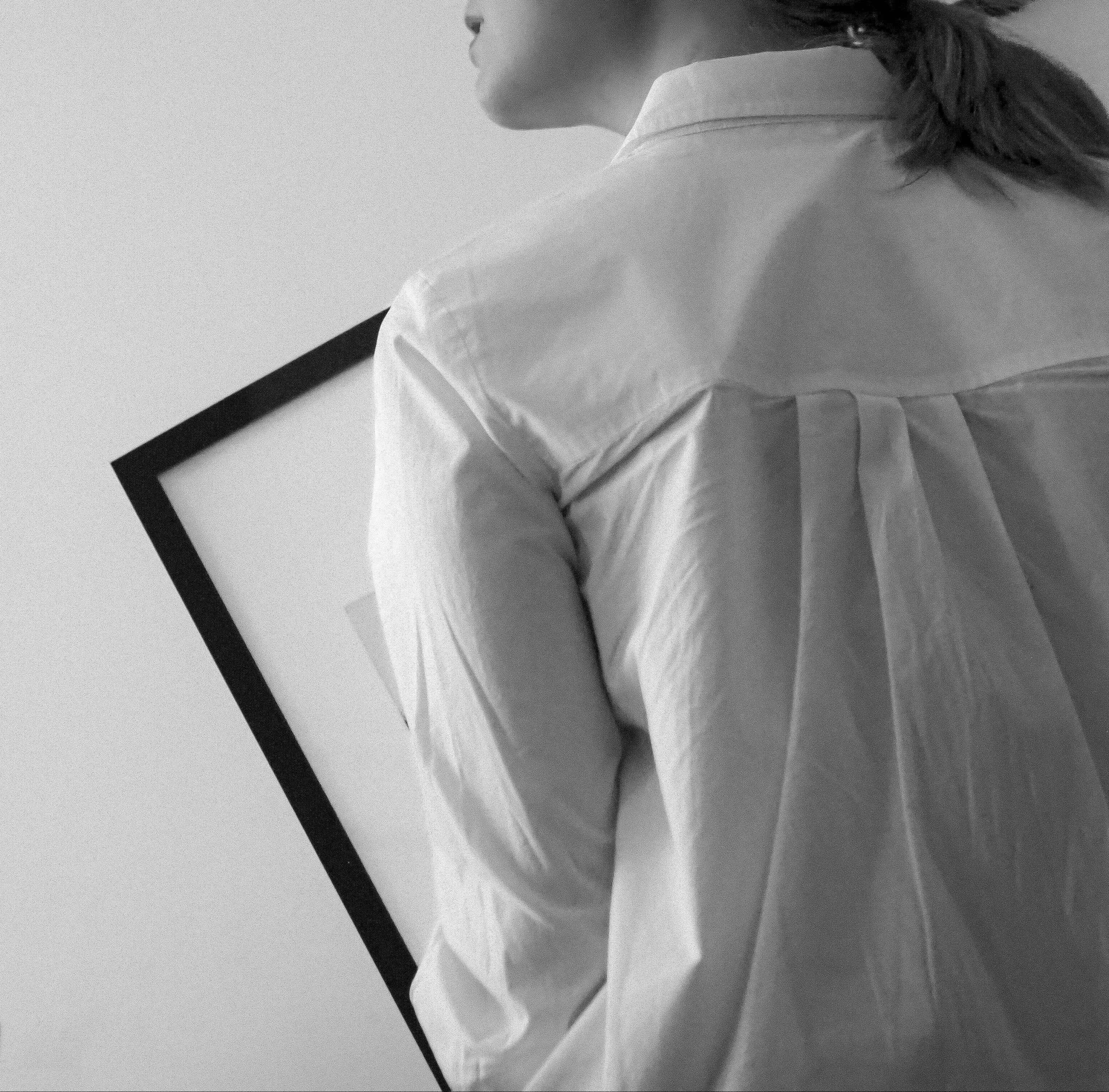 Person wearing a white shirt with a framed picture on a light background